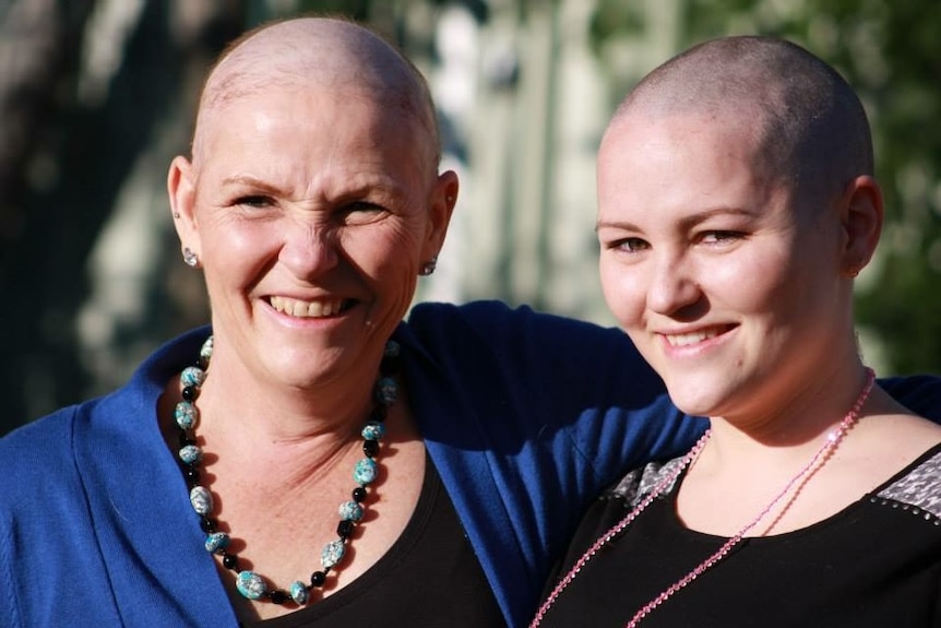 Two women with shaved heads embrace