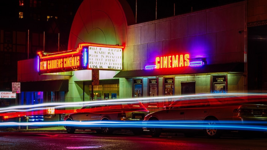 a cinema on s street corner at night lit up with neon signs