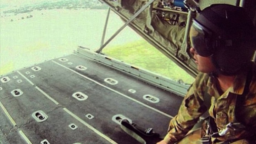 Man with helmet and army clothing sits on the ramp of an aircraft and looks outside