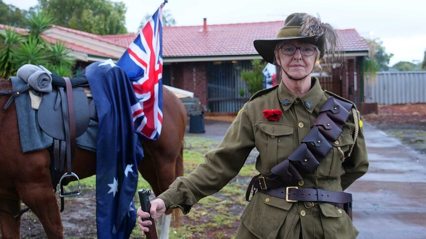 A woman stands on her driveway with her horse and Australian flags