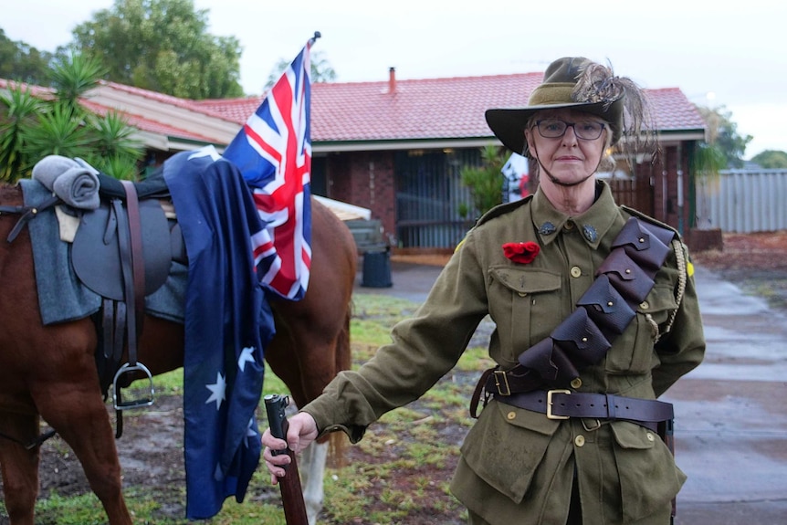 A woman stands on her driveway with her horse and Australian flags
