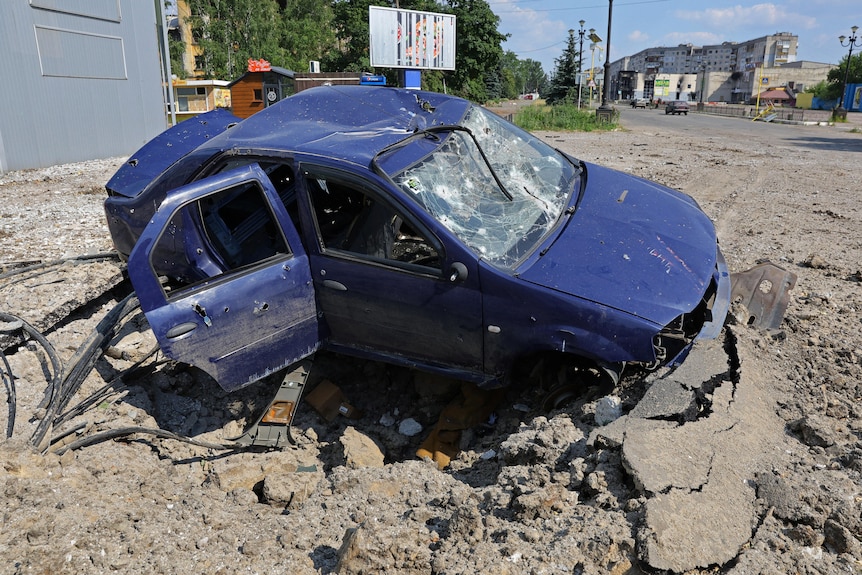 A shattered car in a crater on a street in Ukraine