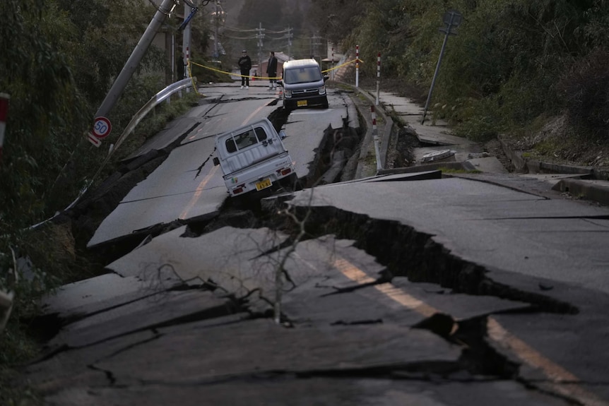 A large crack in a road with two cars on top
