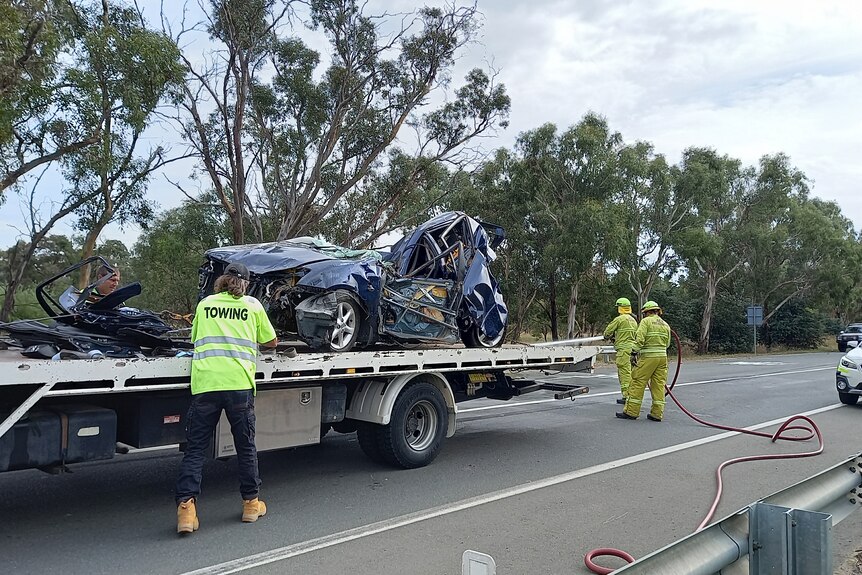 Emergency services load the wreckage of a car onto a tow truck.