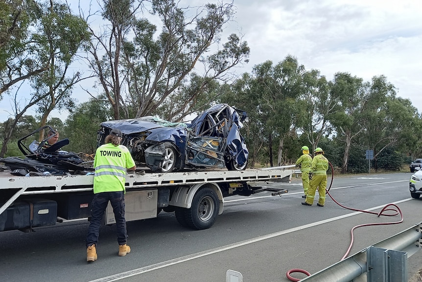 Emergency services load the wreckage of a car onto a tow truck.