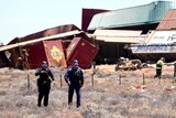 Two police walk in front of cargo pile up with fire fighter in the background closer to the wreckage