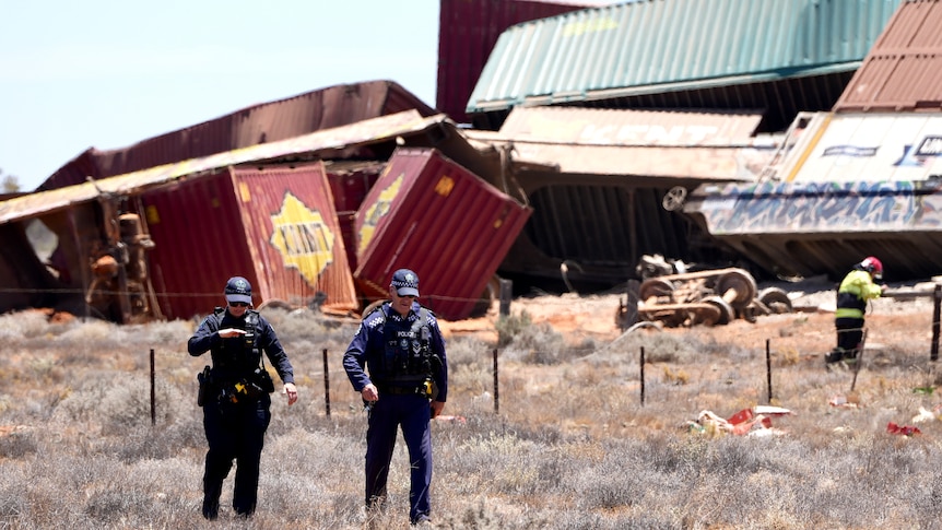 Two police walk in front of cargo pile up with fire fighter in the background closer to the wreckage