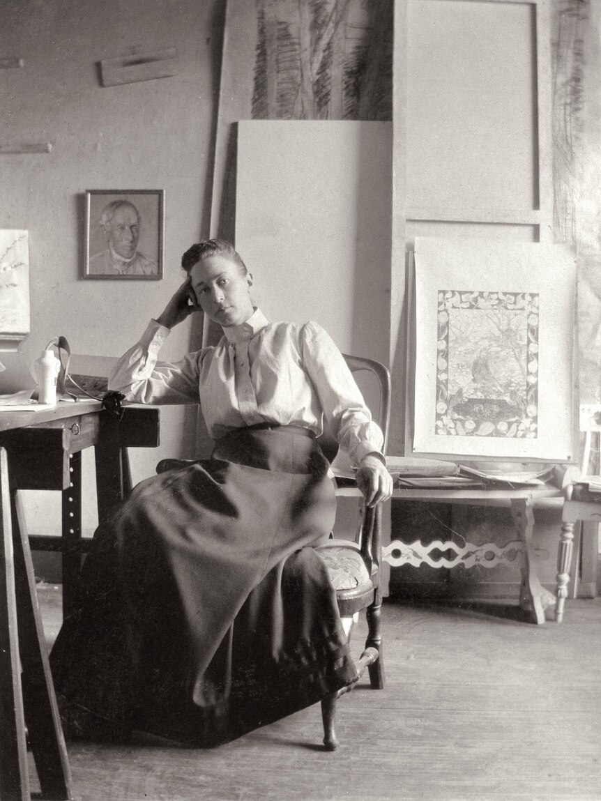 Black and white photo of Hilma af Klint sitting in art studio, with her head resting on her hand. 