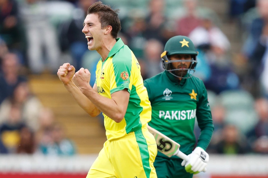 Pat Cummins clenches both fists and yells while a Pakistan batsman stands behind him.