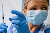 A nurse wearing a face mask and latex gloves prepares to tap a syringe of the Pfizer-BioNTech COVID-19 vaccine