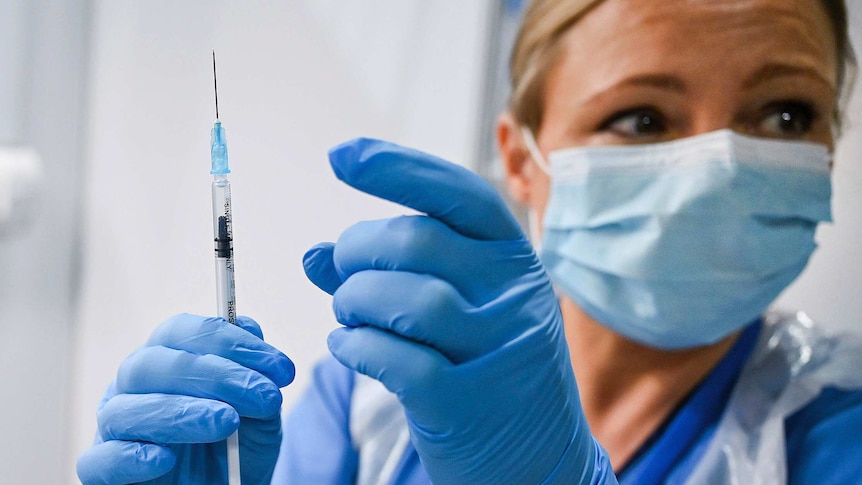 A nurse wearing a face mask and latex gloves prepares to tap a syringe of the Pfizer-BioNTech COVID-19 vaccine