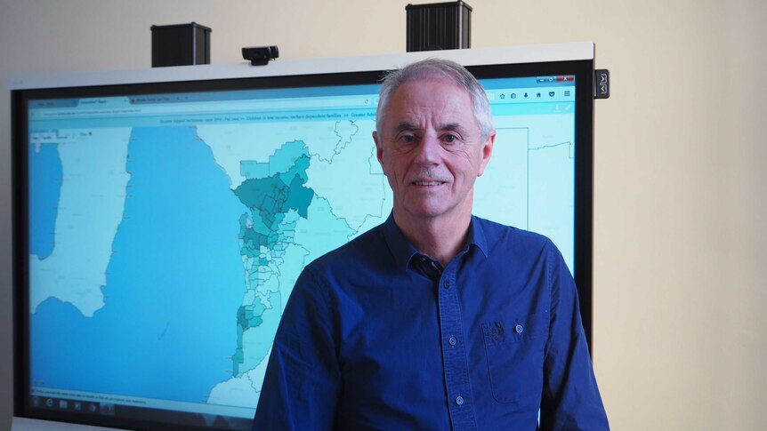 A man looks at the camera while standing in front of a large monitor displaying a map.