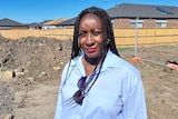 Nathalie Kapuya stands on an a dirt patch, with homes all around her block of empty land