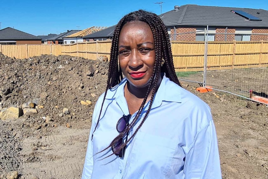 Nathalie Kapuya stands on an a dirt patch, with homes all around her block of empty land
