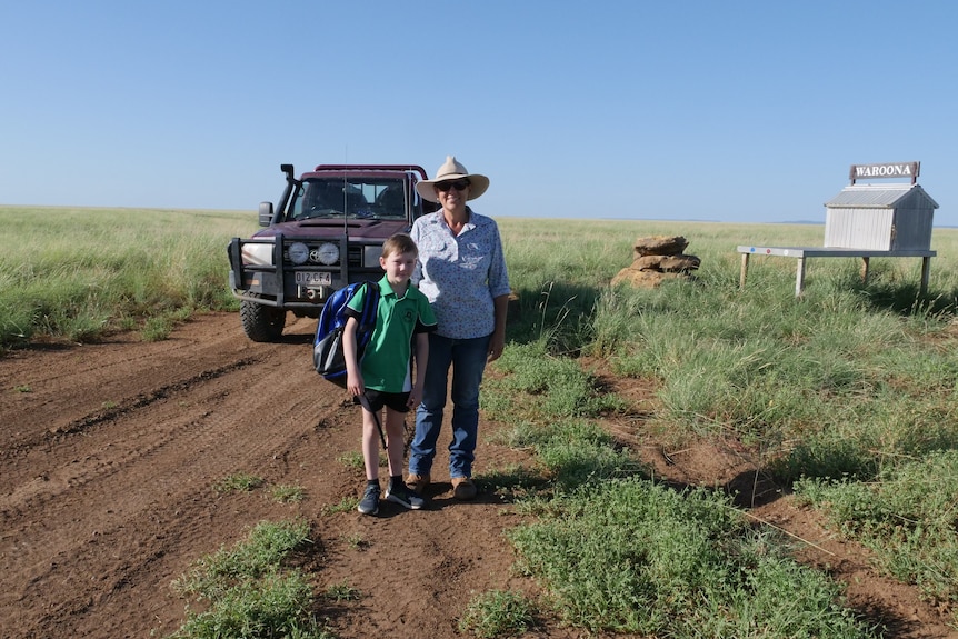 A young boy in a school uniform and mum smile on an outback property.