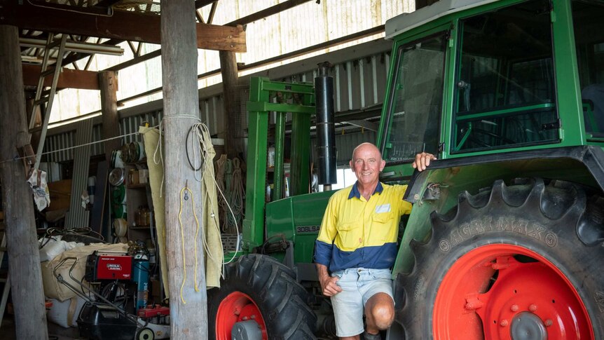 A wide shot of a man in his-vis standing in front of a green tractor in a shed