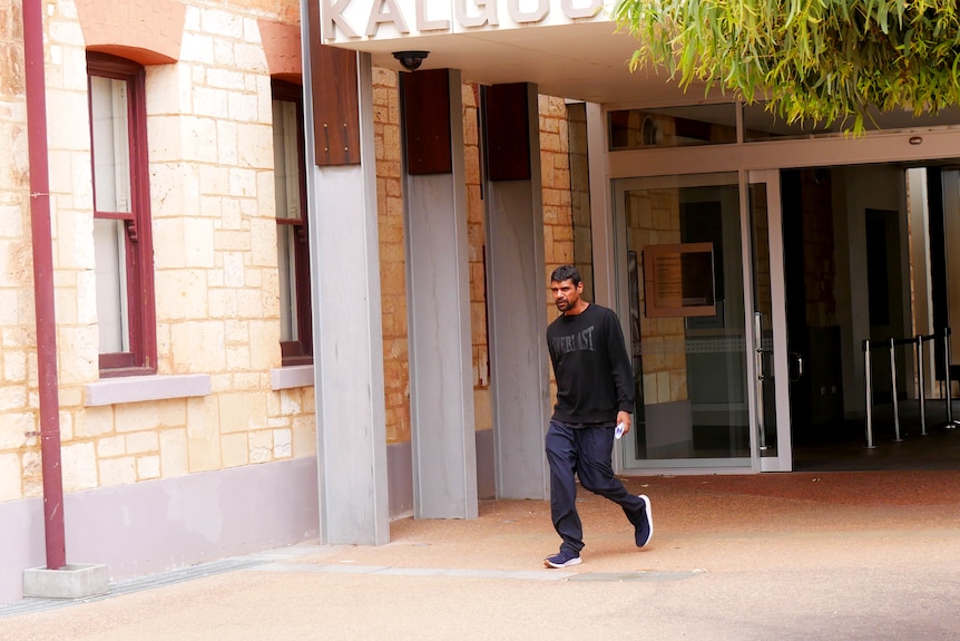 A man wearing a black jumper and tracksuit pants leaves court. 