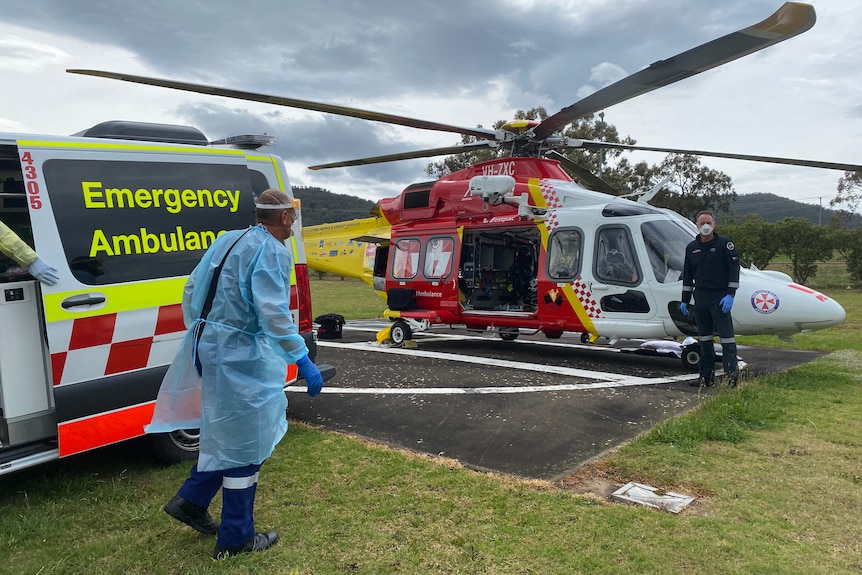 A person in PPE stands near a rescue helicopter.