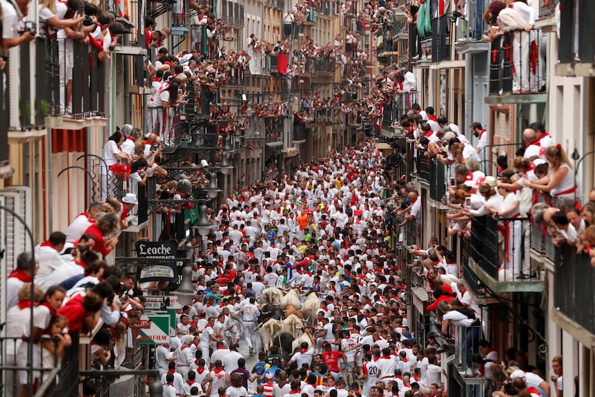 Revellers sprint in front of bulls in a street crowded with people watching from balconies.