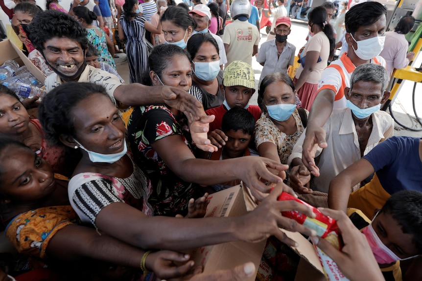 A crowd of people jostle to get closer to a person handing out packets of biscuits