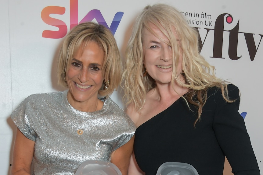 Two women in formal dress smile as they pose with awards