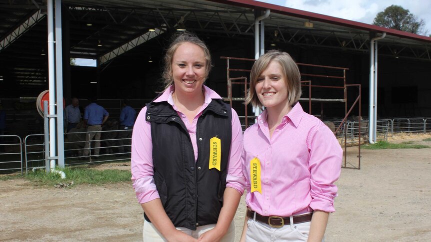 Peta Bradley and Jo Newton stand outside of the sheep show wearing pink shirts and yellow steward ribbons.
