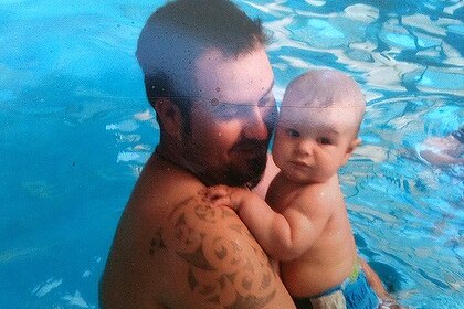 A man holding his baby son in a swimming pool.  