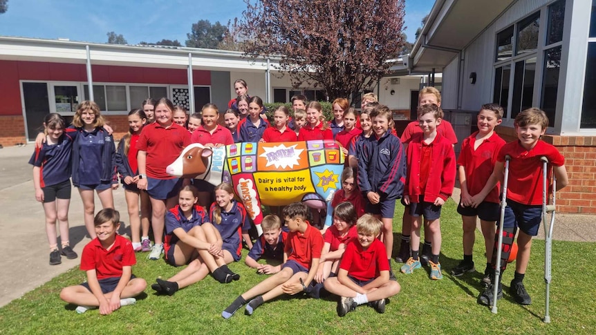 A group of primary school students in red uniforms stand smiling in front of their life-size painted cow.
