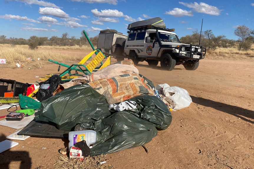 a pile of plastic garbage bags next to a dirt road