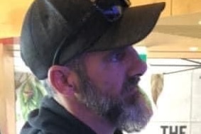 Side profile of a man with a grey beard wearing a black cap