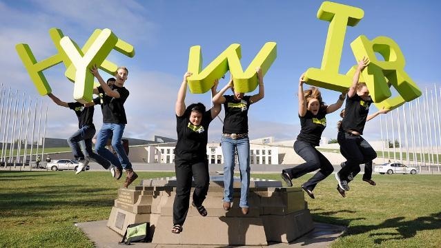 Teenagers jump holding big letters to spell out 'Heywire', in front of Parliament House in Canberra