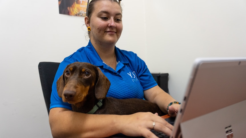 Rikki Hoyland sits with her dog on her lap as she types.