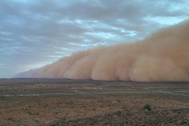 Large clouds of red dust roll over the desert landscape