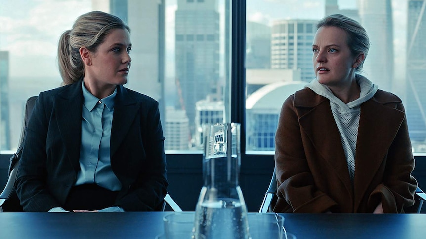 Two women sit at a desk in an office building
