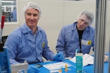 Two scientists in lab coats and hair nets sitting at a desk.