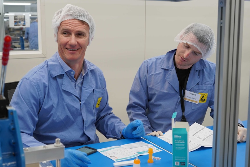 Two scientists in lab coats and hair nets sitting at a desk.