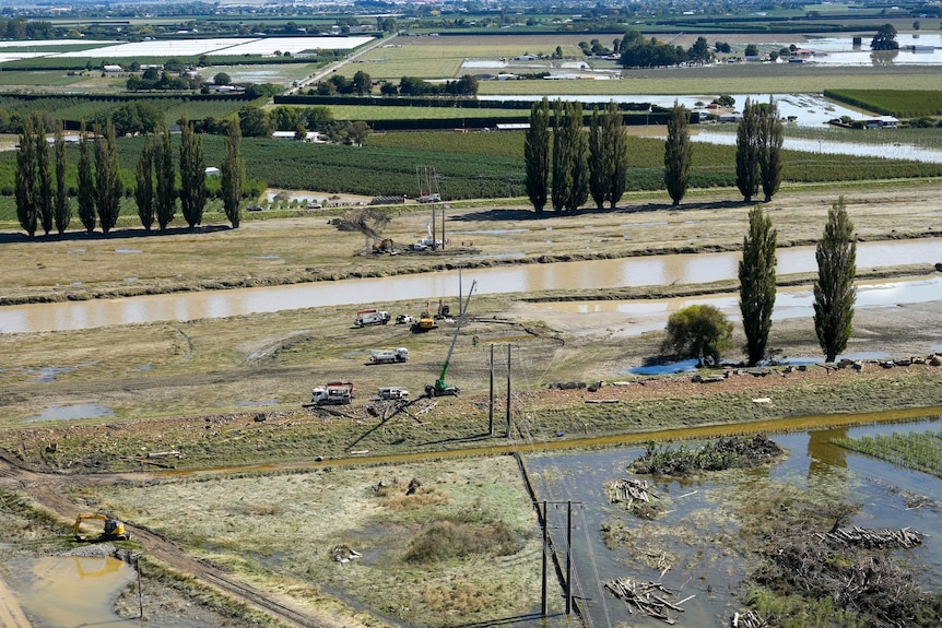 A view showing fields with some powerlines down and water surrounding them. 