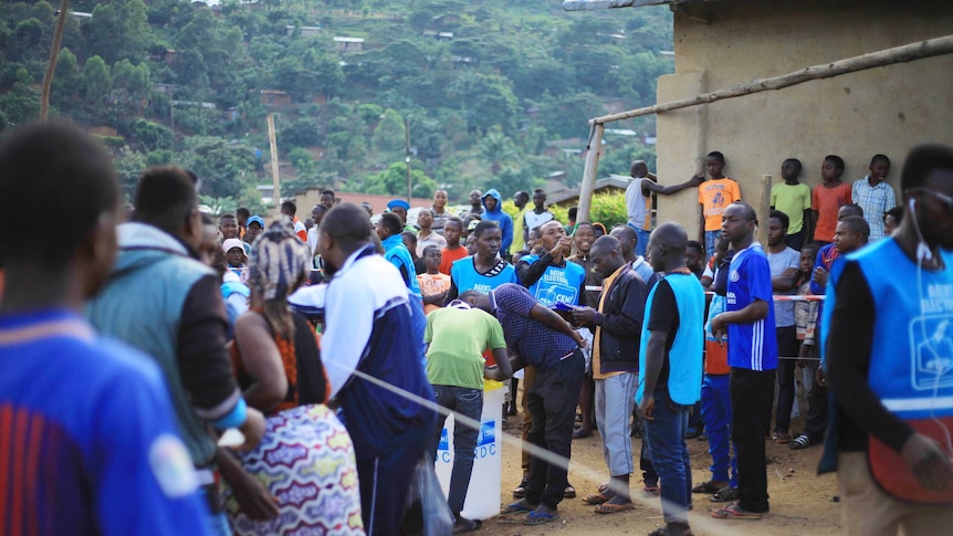 Crowds of Congolese people, many in blue vests, congregate around a plastic tub where people are casting votes.