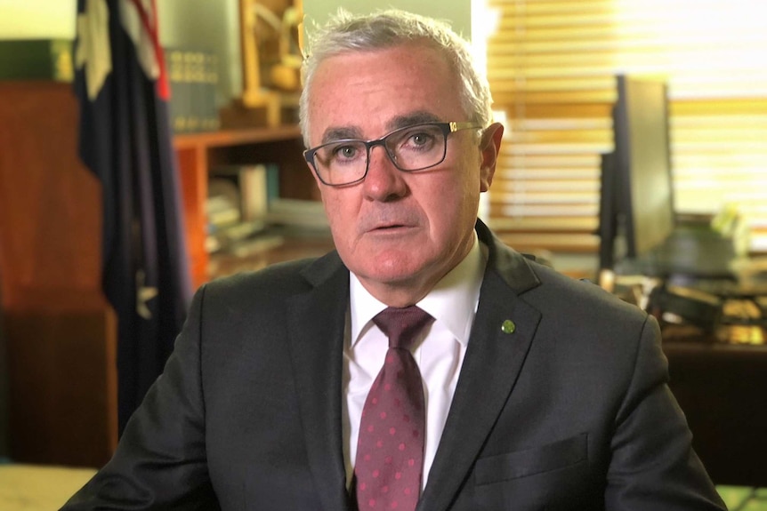 Andrew sits in front of a computer monitor and Australian flag.