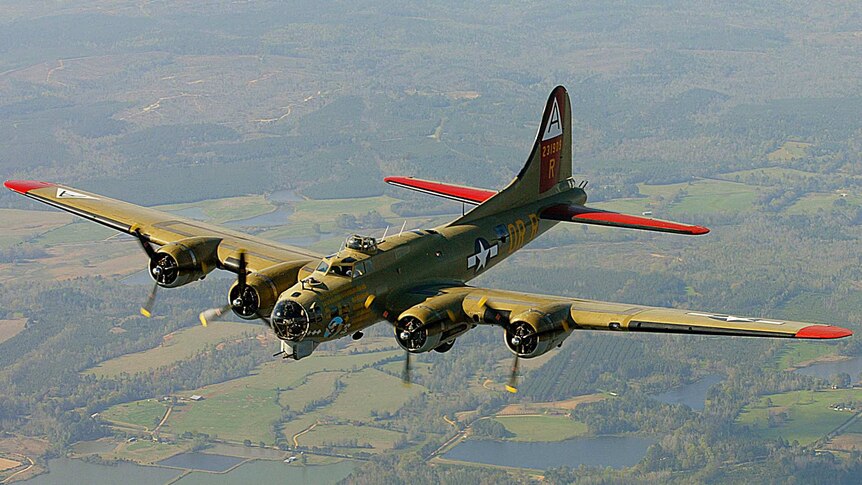 A Collings Foundation B-17 Flying Fortress, green with red wind tips, flies over farmland
