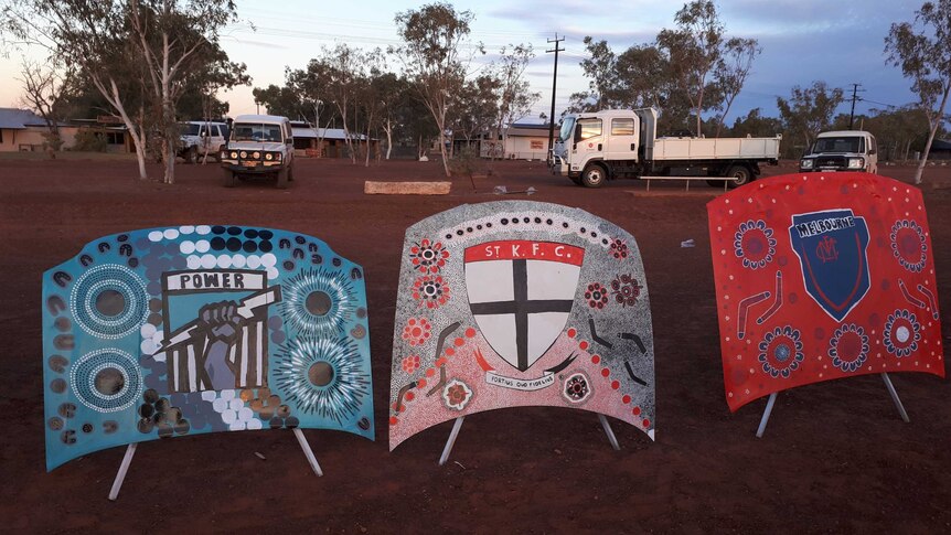 three bonnets lined up next to each other, painted in AFL colours