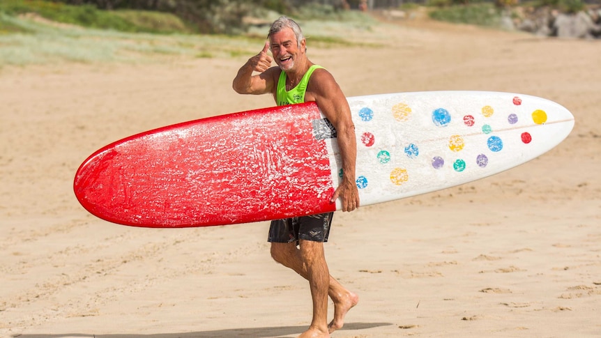 Tanned man on beach with large, spotty surfboard