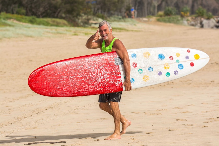 Tanned man on beach with large, spotty surfboard