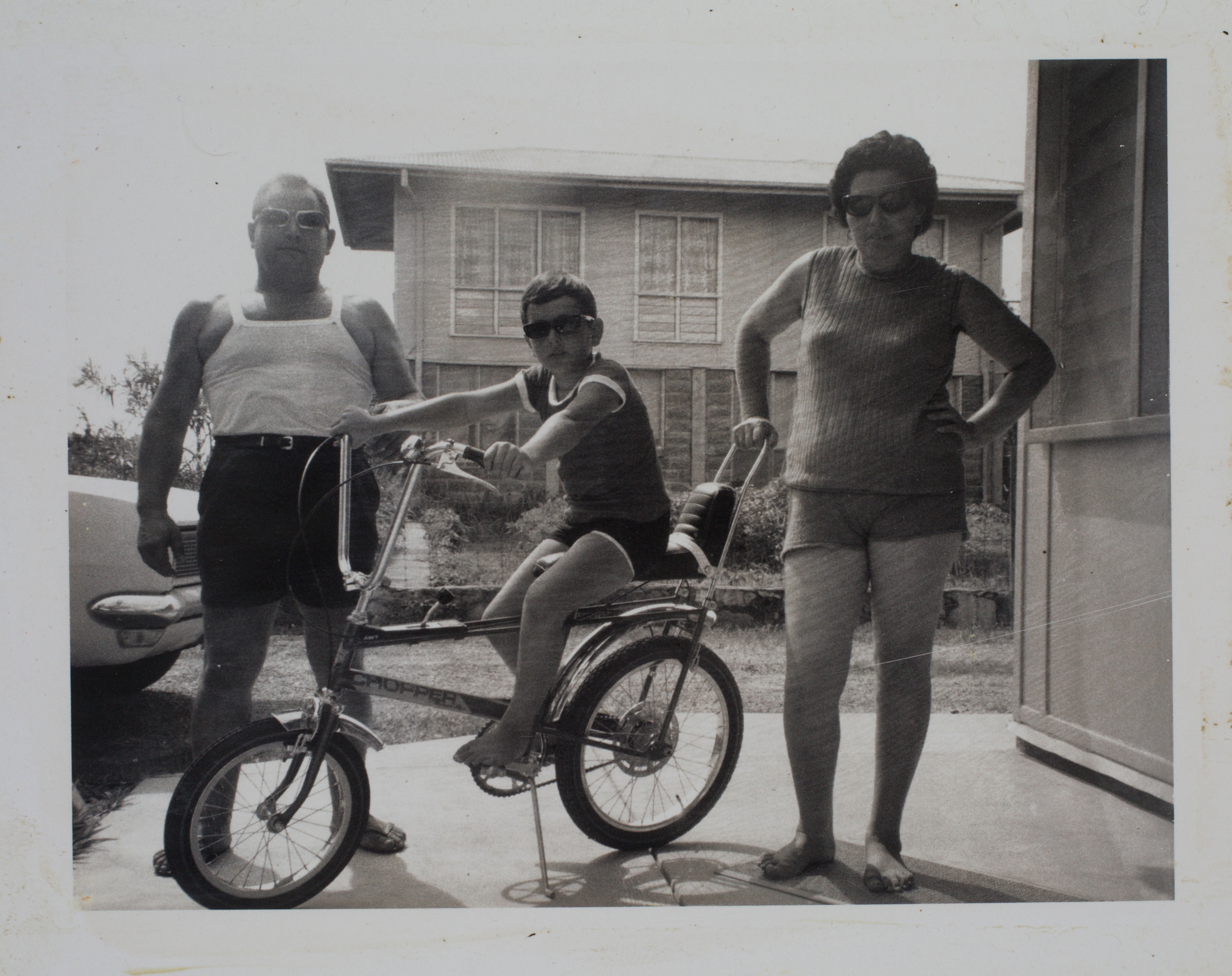 a boy sitting on a bike next to his parents in the 1970s