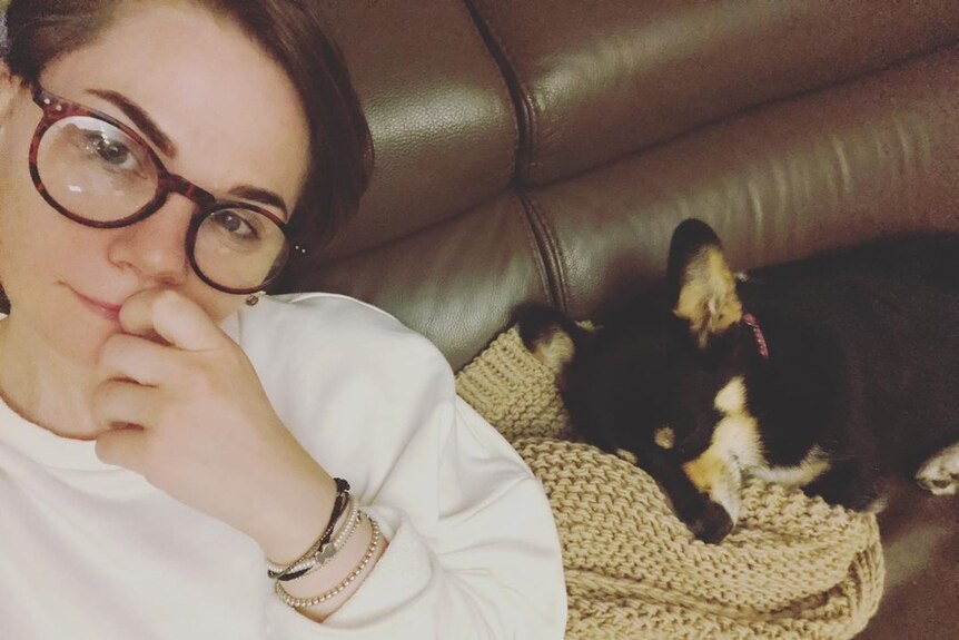 A woman with glasses sitting next to a sleeping dog