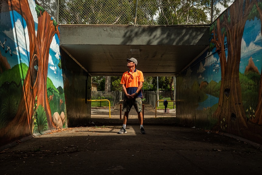 a man looking left stands between two walls painted with trees