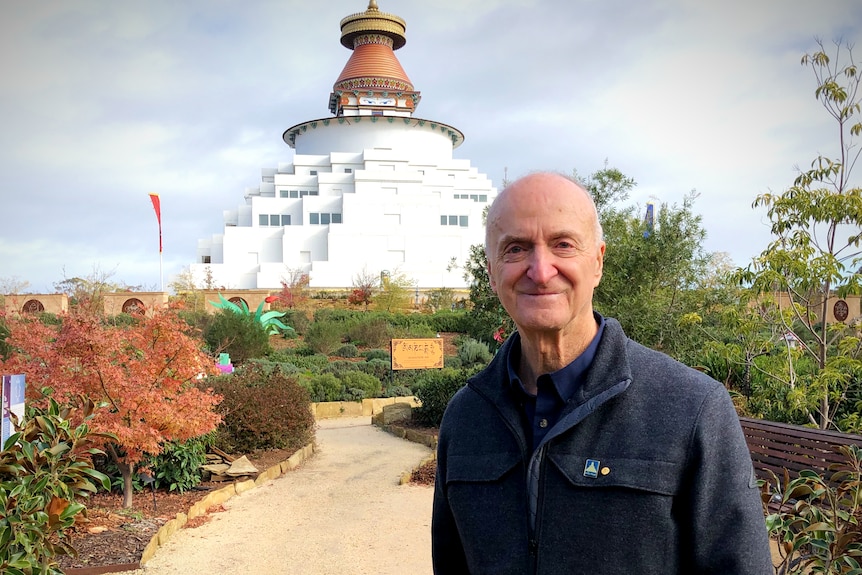 a balding man smiles at the camera in front of a temple