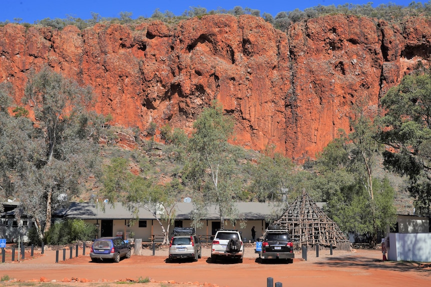 A car park at an outback resort with a red cliff in background.