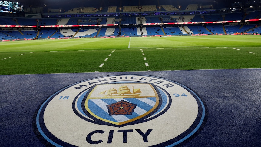 The club emblem of Manchester City is shown in the foreground with its stadium in the background