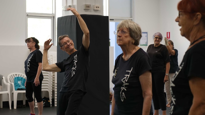 Dance studio rehearsal, Mr Butler standing in the centre with arms stretched above his head.